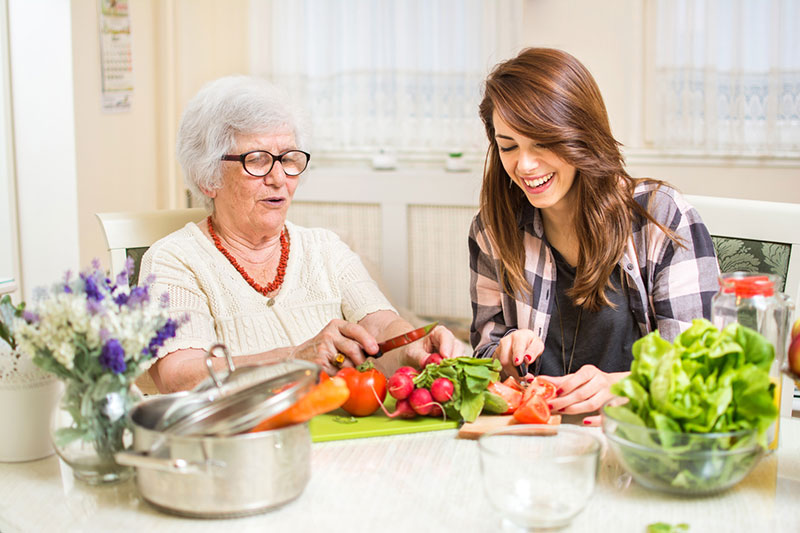 Polnische Haushaltshilfe unterstützt ältere Frau zu Hause beim Kochen und Zubereiten von Speisen.